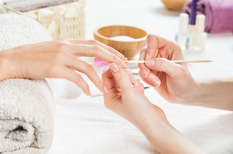 Closeup shot of a woman using a cuticle pusher to give a nail manicure. Nail technician giving customer a manicure at nail salon. Young caucasian woman receiving a french manicure.